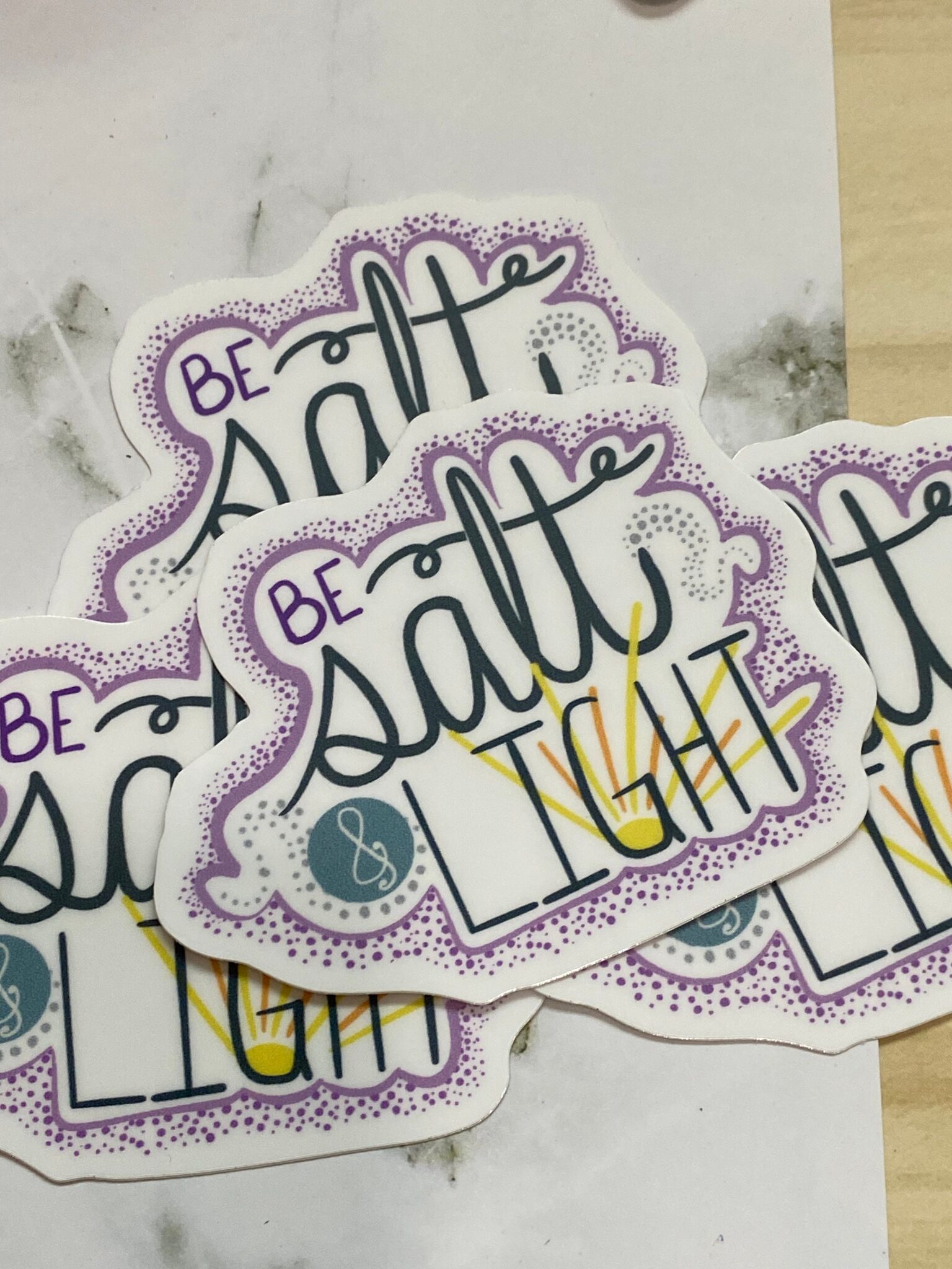 Stickers with the phrase Be Salt & Light in decorative lettering on marble and wood surface.