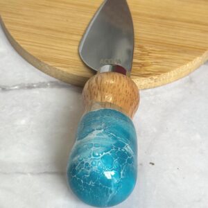 Cheese knife with blue resin and wooden handle on round wooden cutting board.