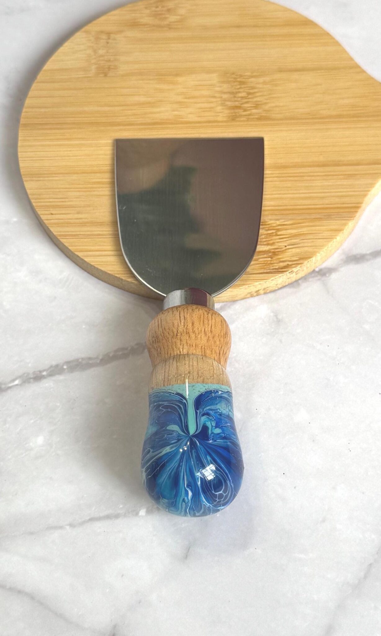 Cheese knife with wooden and blue marbled handle on round wooden cutting board on marble surface