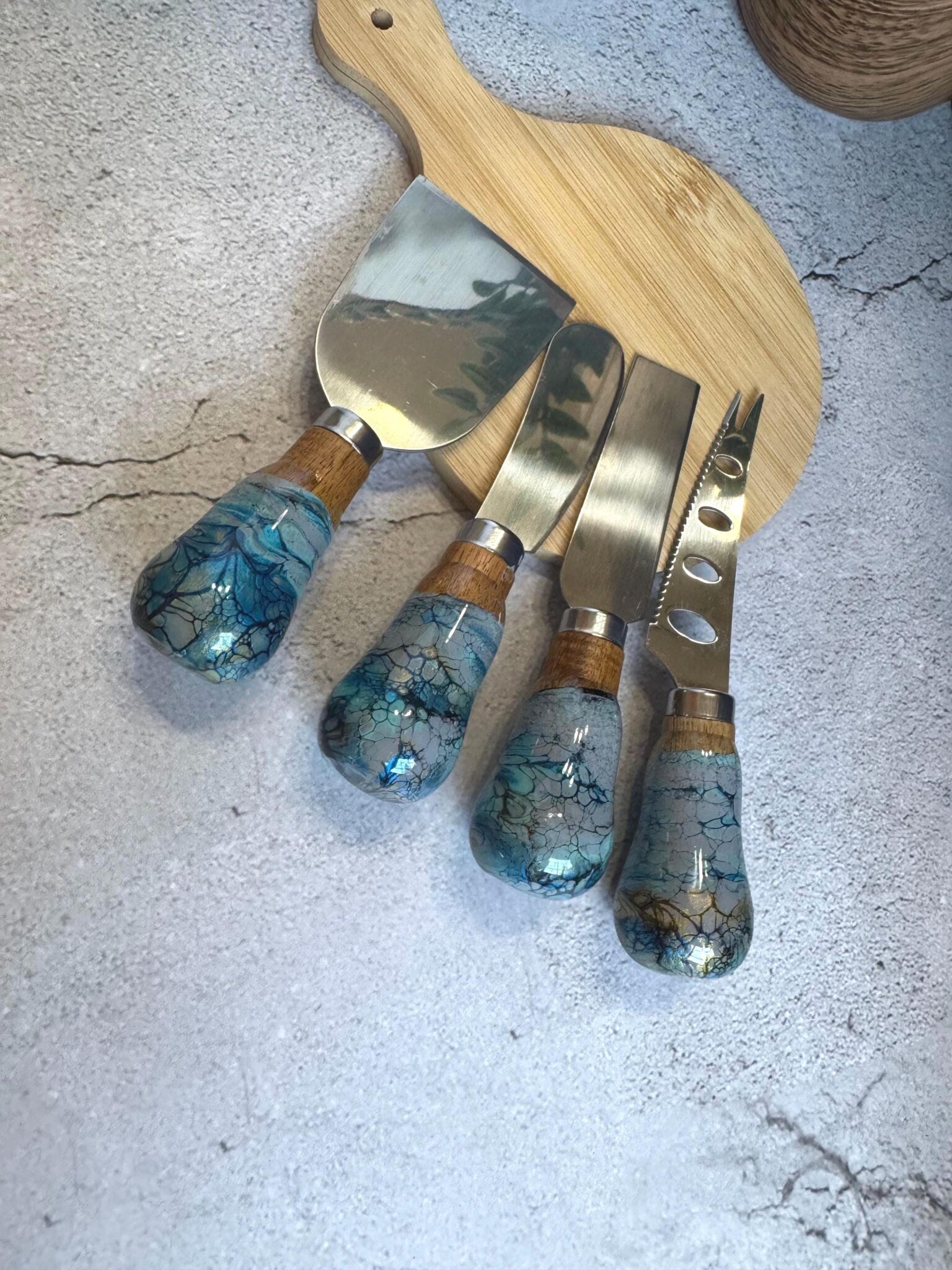 Set of four cheese knives with stainless steel blades and blue marbled handles on wooden board.
