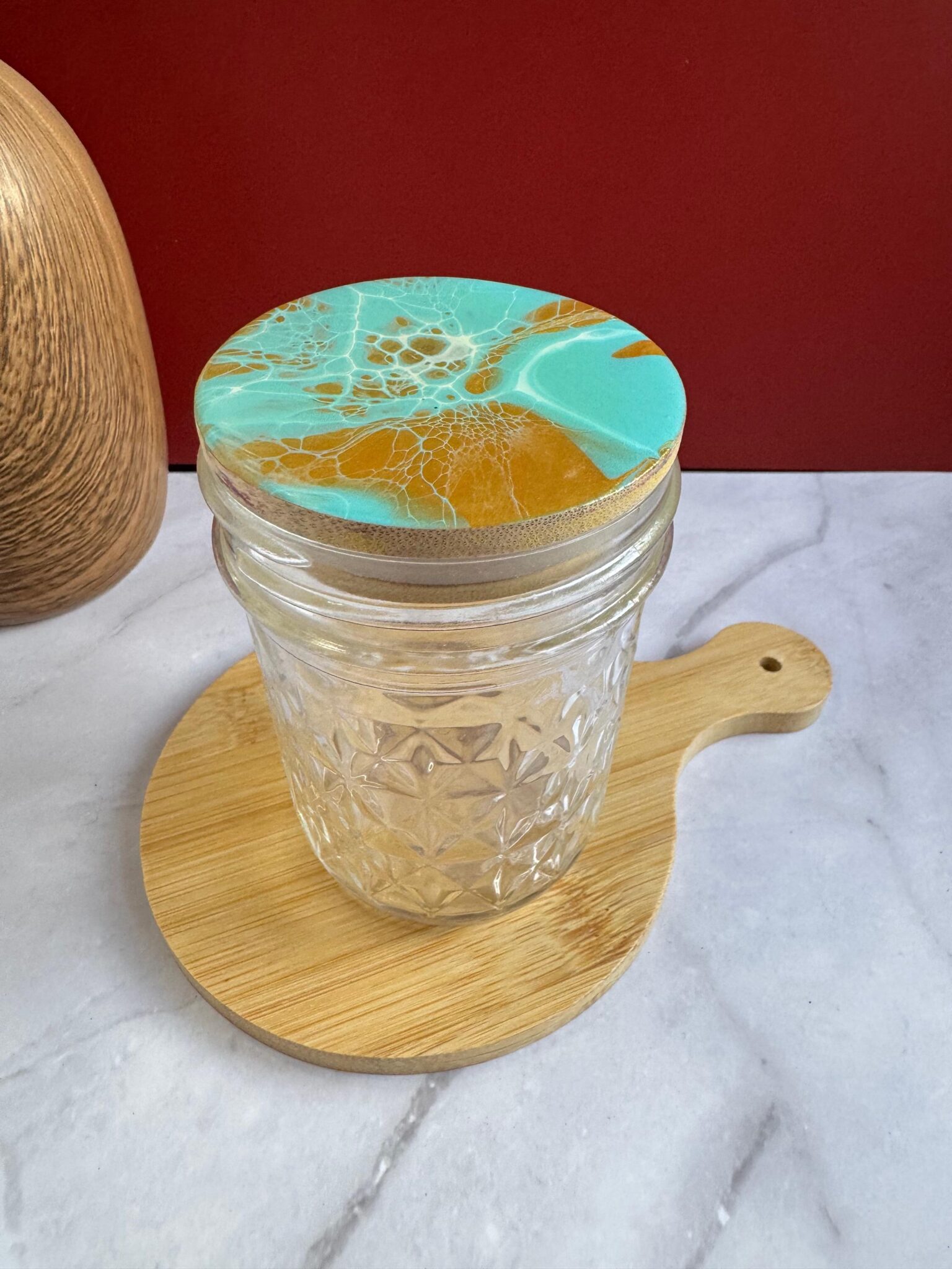 Clear textured glass jar with turquoise and gold marbled lid on round wooden board on marble surface