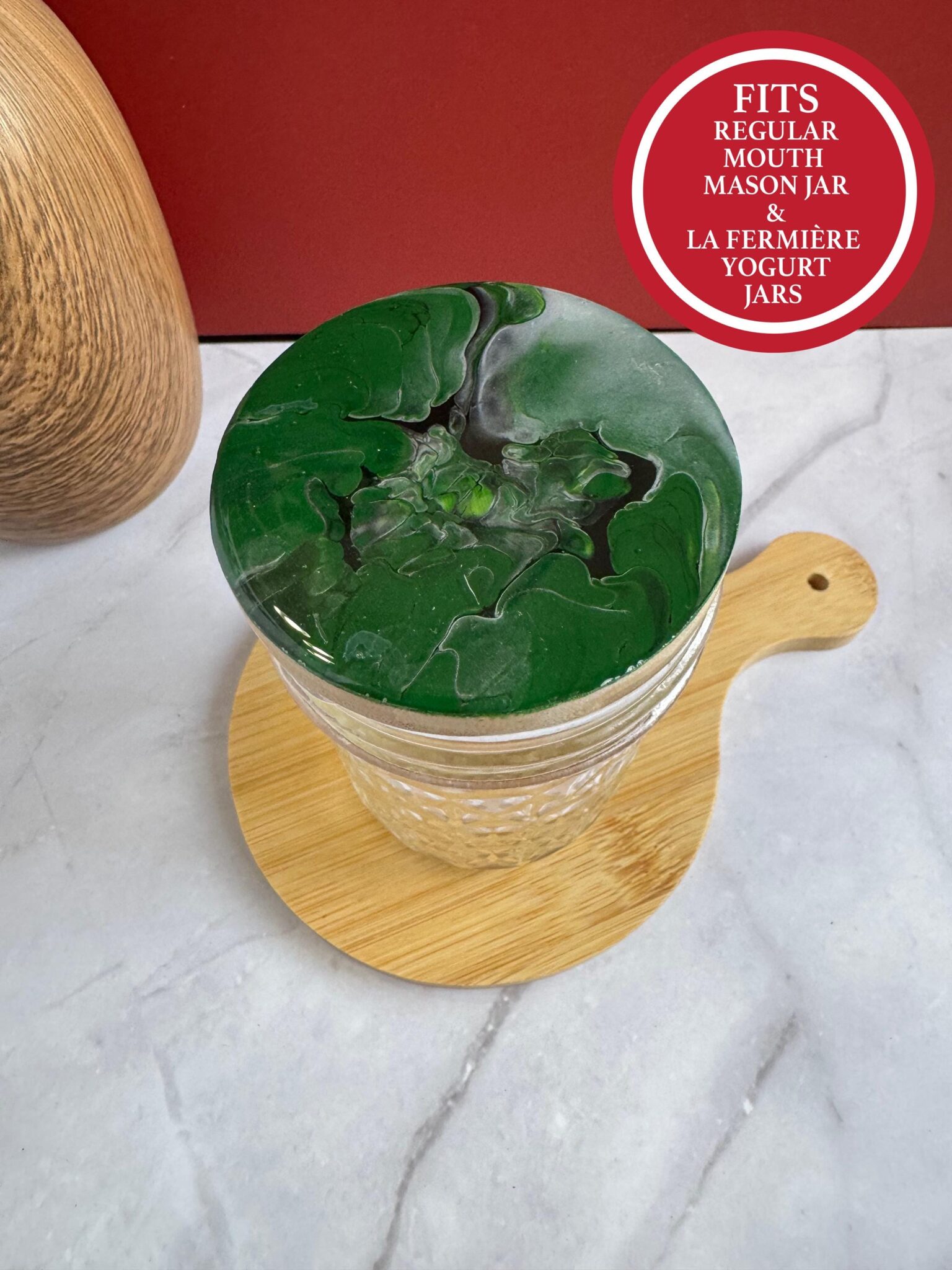 Glass jar with green and gray marbled lid on wooden board near red label about lid fit.