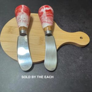 Two spreader knives with red and white marbled handles on a small wooden cutting board.