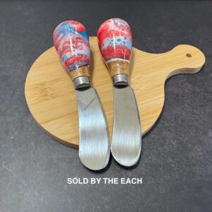 Two cheese spreader knives with red, white, and blue handles on a wooden cutting board.
