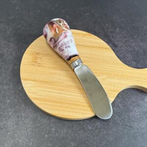 Small wooden cutting board with handle and spreader knife with marbled handle on gray surface