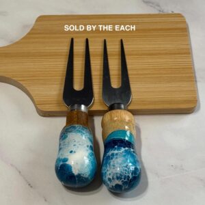 Two cheese forks with blue and white marbled wooden handles on a bamboo cutting board.
