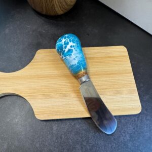 Wooden cutting board on dark countertop with a butter knife featuring a blue and white handle.