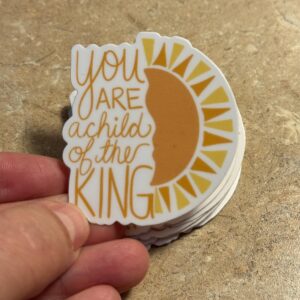 Hand holding stacked stickers with a yellow sun graphic and text you are a child of the king.