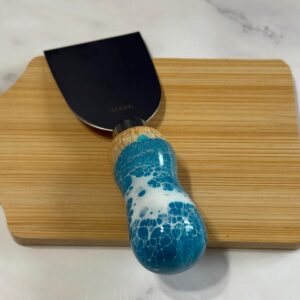 Wooden cutting board with a putty knife featuring a black blade and blue-white marbled handle.