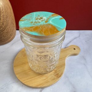 Clear textured glass jar with turquoise and gold marbled lid on round wooden board on marble surface