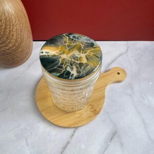 Clear textured glass jar with marbled lid on wooden board against red background.