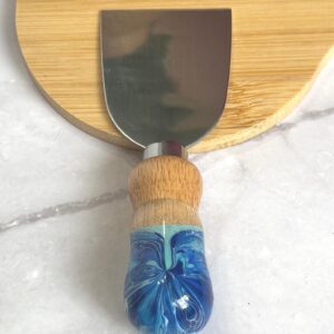 Cheese knife with wooden and blue marbled handle on round wooden cutting board on marble surface
