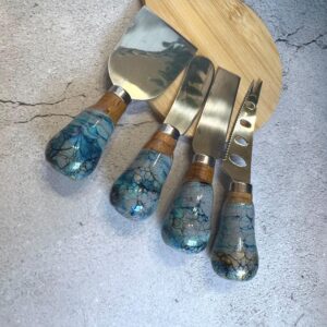 Set of four cheese knives with stainless steel blades and blue marbled handles on wooden board.