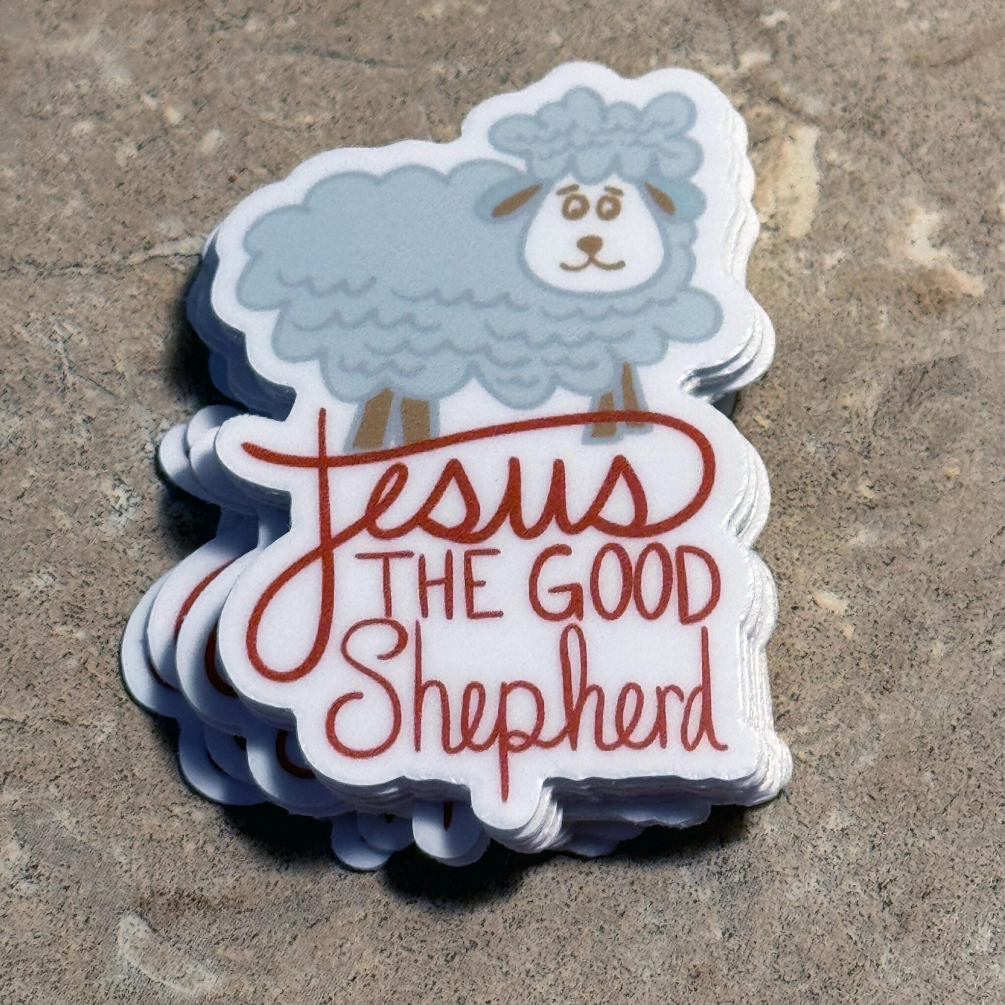 Stack of stickers with cartoon sheep and text Jesus The Good Shepherd on textured surface