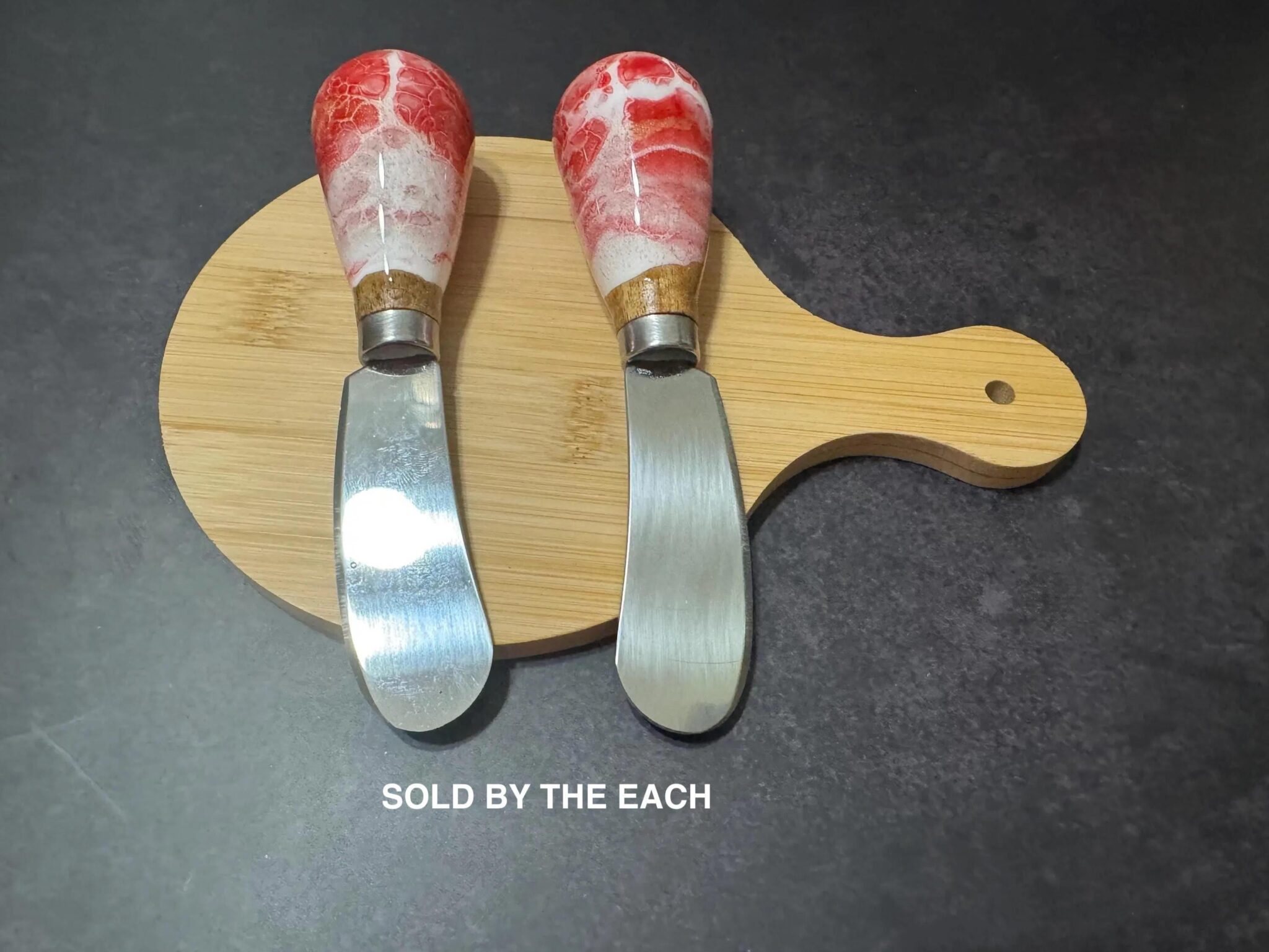 Two spreader knives with red and white marbled handles on a small wooden cutting board.