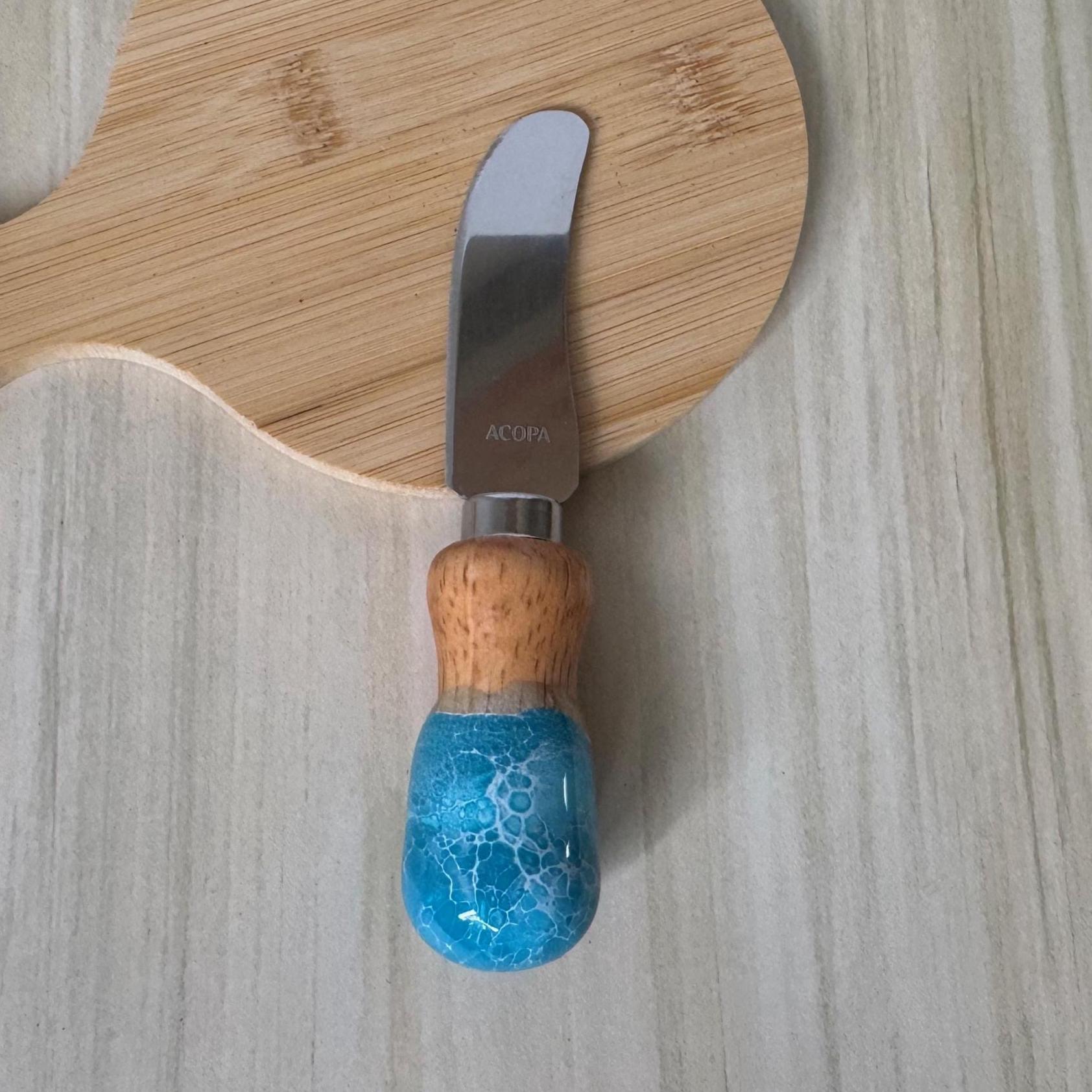 Small cheese knife with wooden and blue resin handle on light wood surface and cutting board