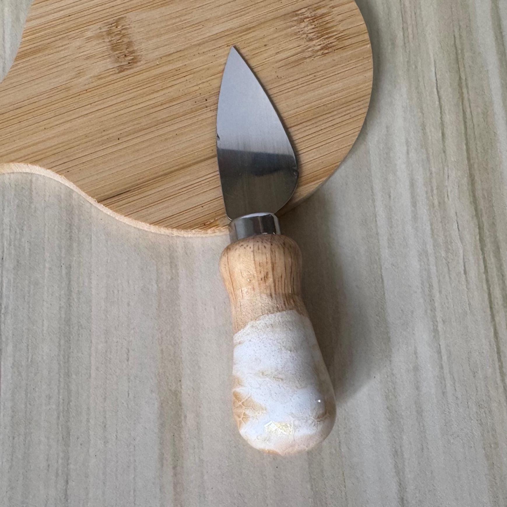 Small cheese knife with curved stainless blade and wooden white handle on wooden surface.