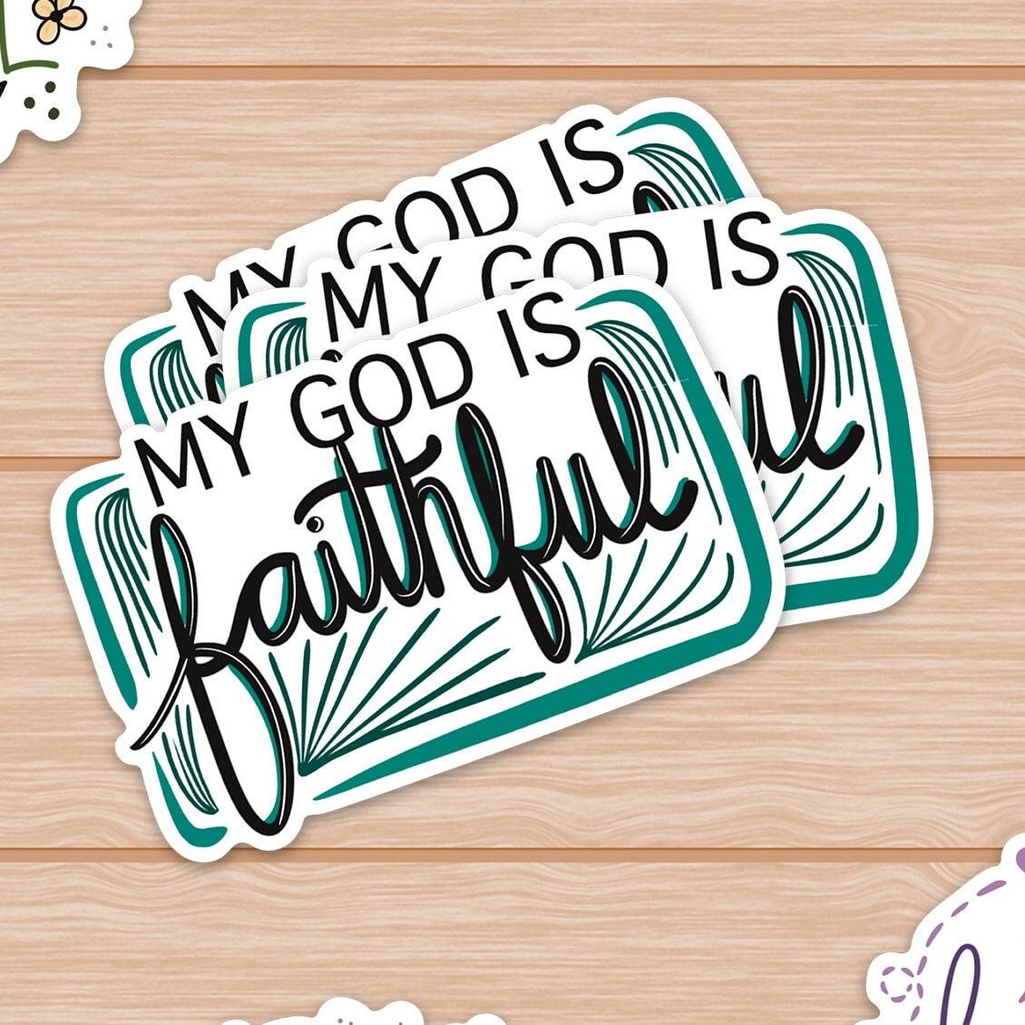 Stacked stickers on wood with the phrase My God Is Faithful in black and teal.