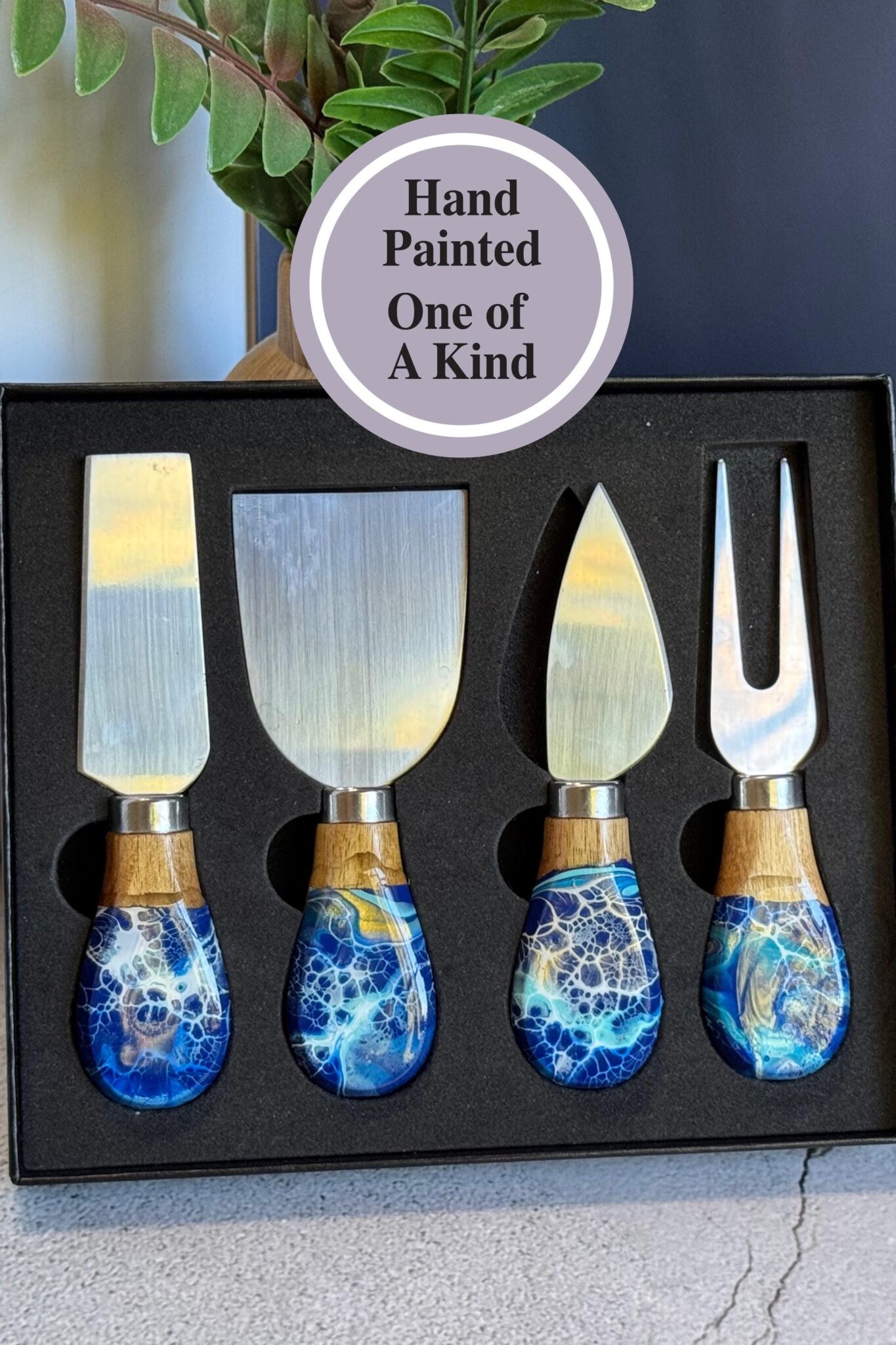 Set of four stainless steel cheese knives with blue and white hand-painted handles in a black box.