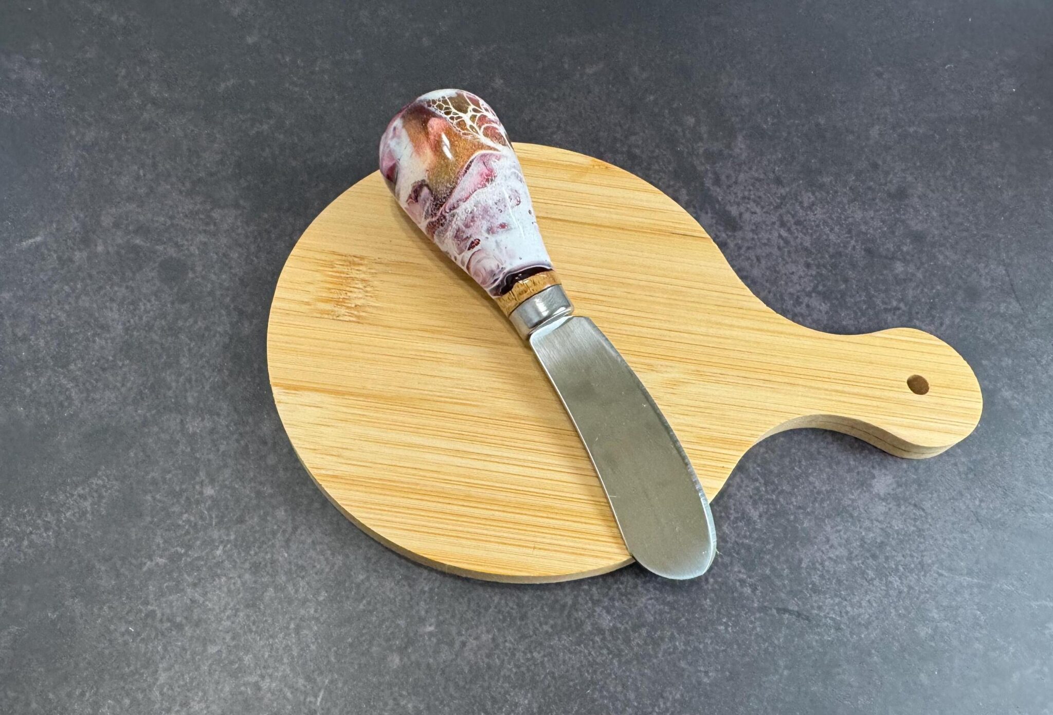 Small wooden cutting board with handle and spreader knife with marbled handle on gray surface