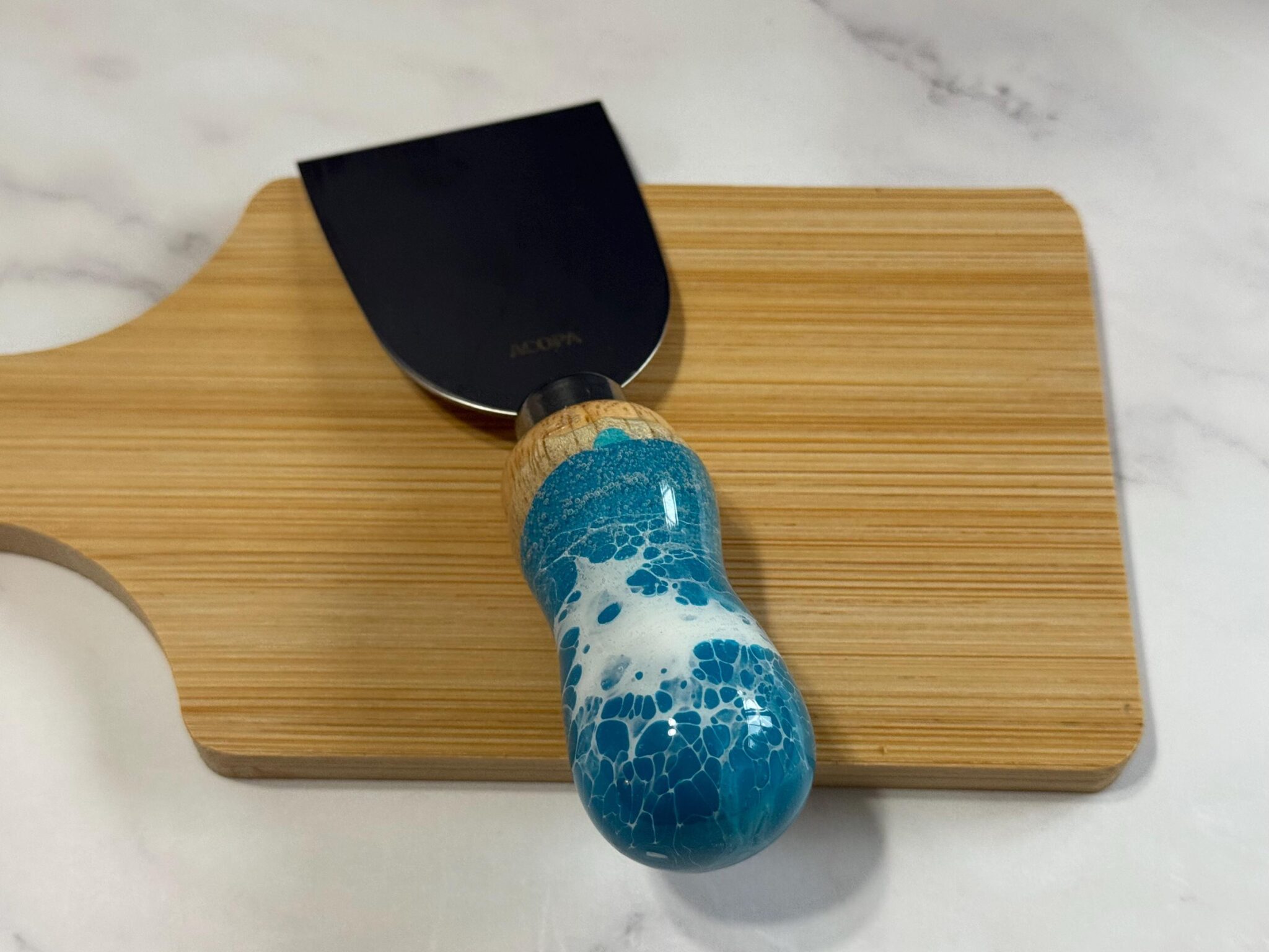Wooden cutting board with a putty knife featuring a black blade and blue-white marbled handle.