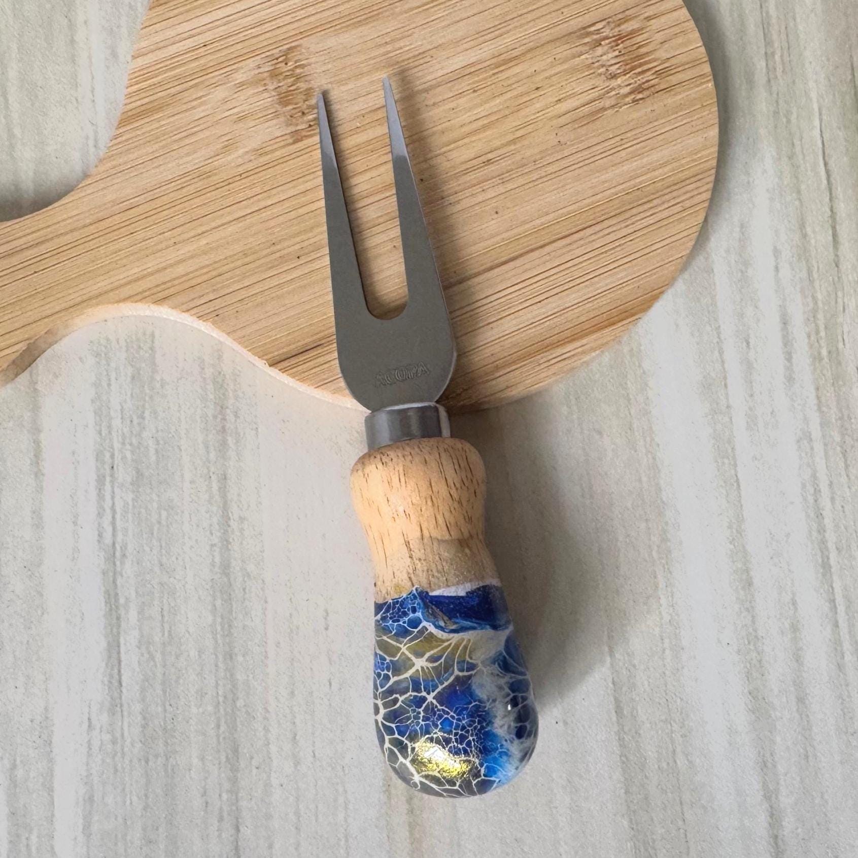 Small two-pronged fork with wooden handle decorated in blue, white, and gold on a light surface.